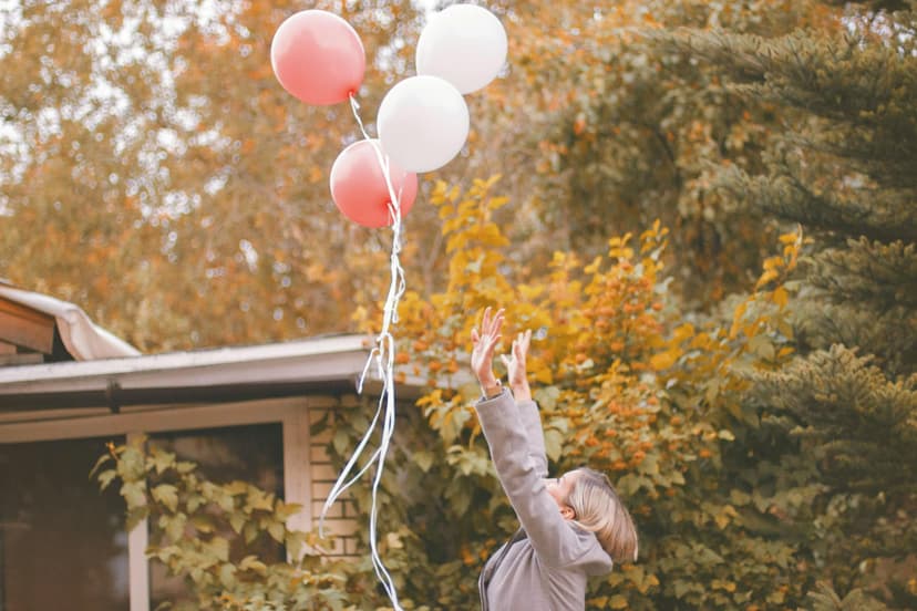 Niña en un bosque cerca de una casa con los brazos extendidos al haber liberado unos globos