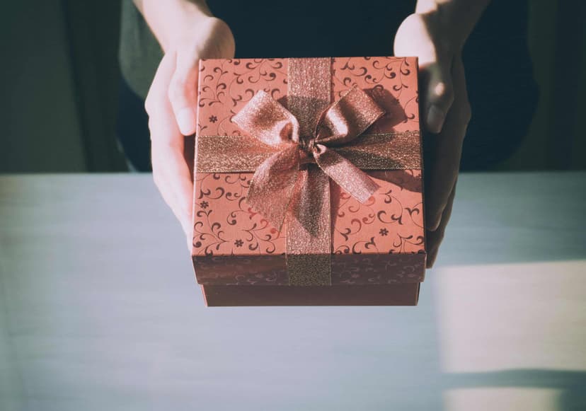 Mano entregando un regalo en una caja roja con estampado de flores