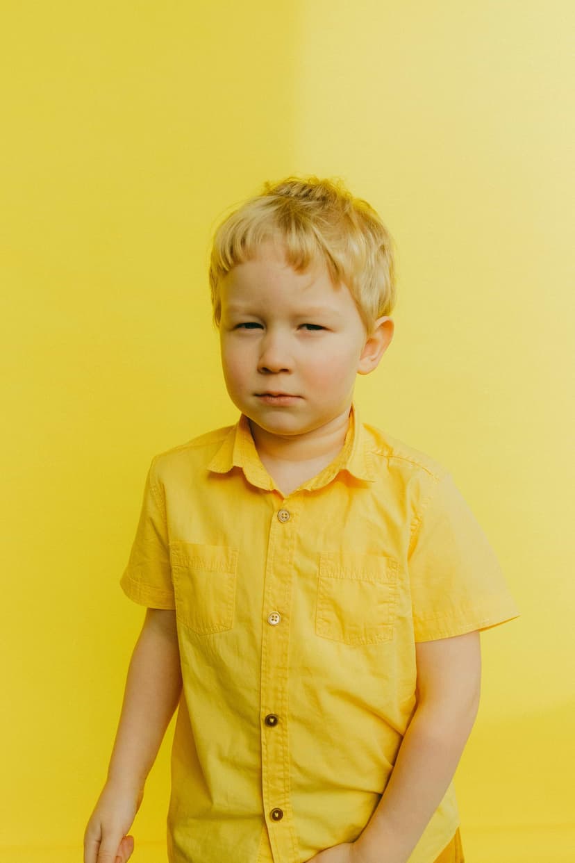 Niño En Camisa Amarilla Con Botones De Pie Junto A La Pared Sospechando